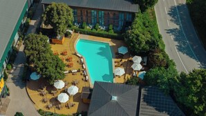 A rooftop pool with sun loungers and umbrellas, surrounded by trees and a building.