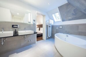 A modern bathroom with a large bathtub, dual sinks, and a skylight. - Ringhotel Waldhotel Heiligenhaus (Heiligenhaus)