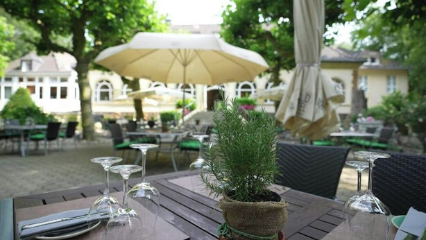 An outdoor dining area with tables, chairs, and a potted plant. - Ringhotel Waldhotel Heiligenhaus (Heiligenhaus)