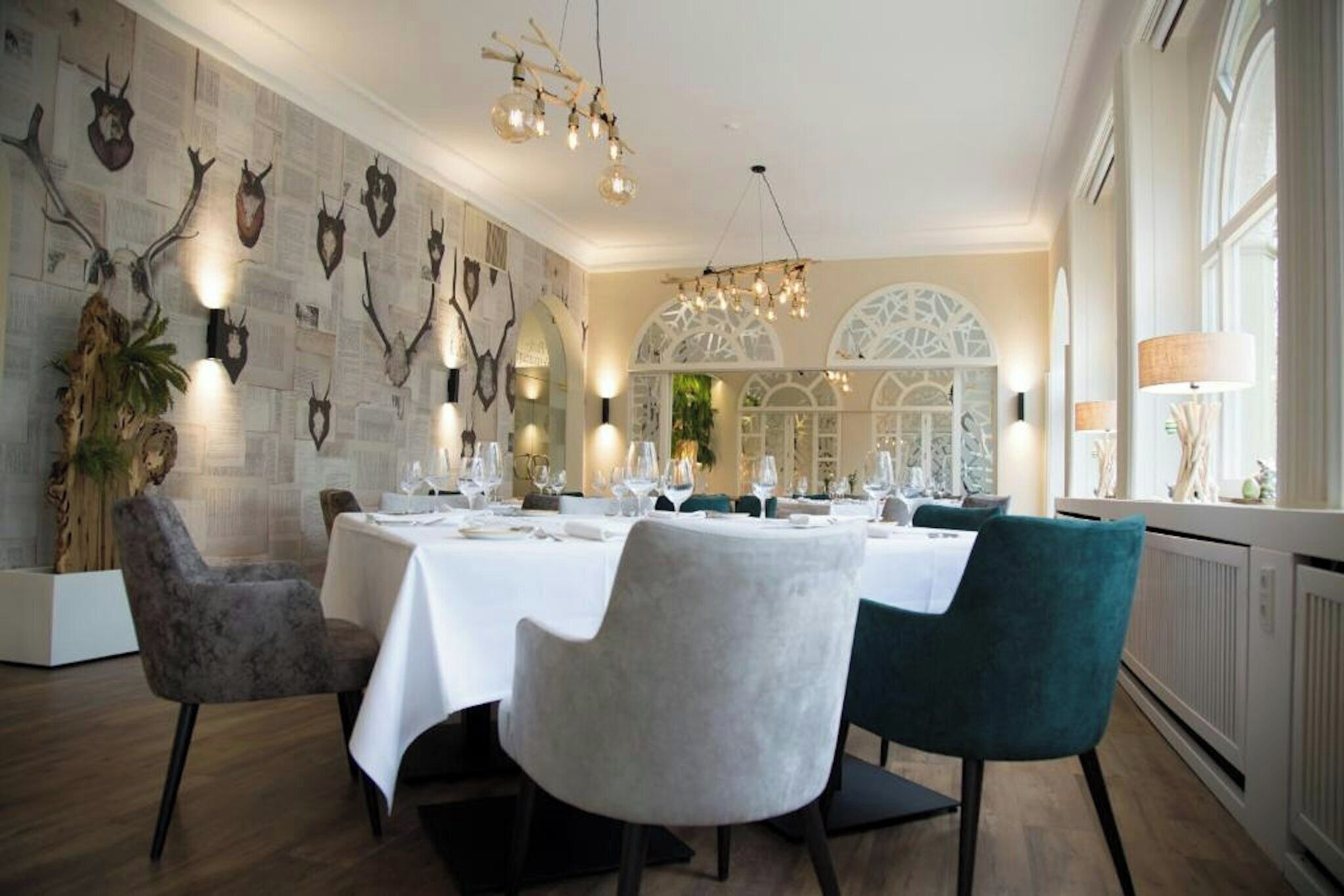 Un coin repas avec une nappe blanche, des chaises de couleur turquoise et des crânes d’animaux accrochés au mur.