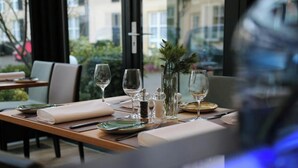 A restaurant table set with plates, glasses, and cutlery, with a view of buildings and greenery outside. - Ringhotel Waldhotel Heiligenhaus (Heiligenhaus)