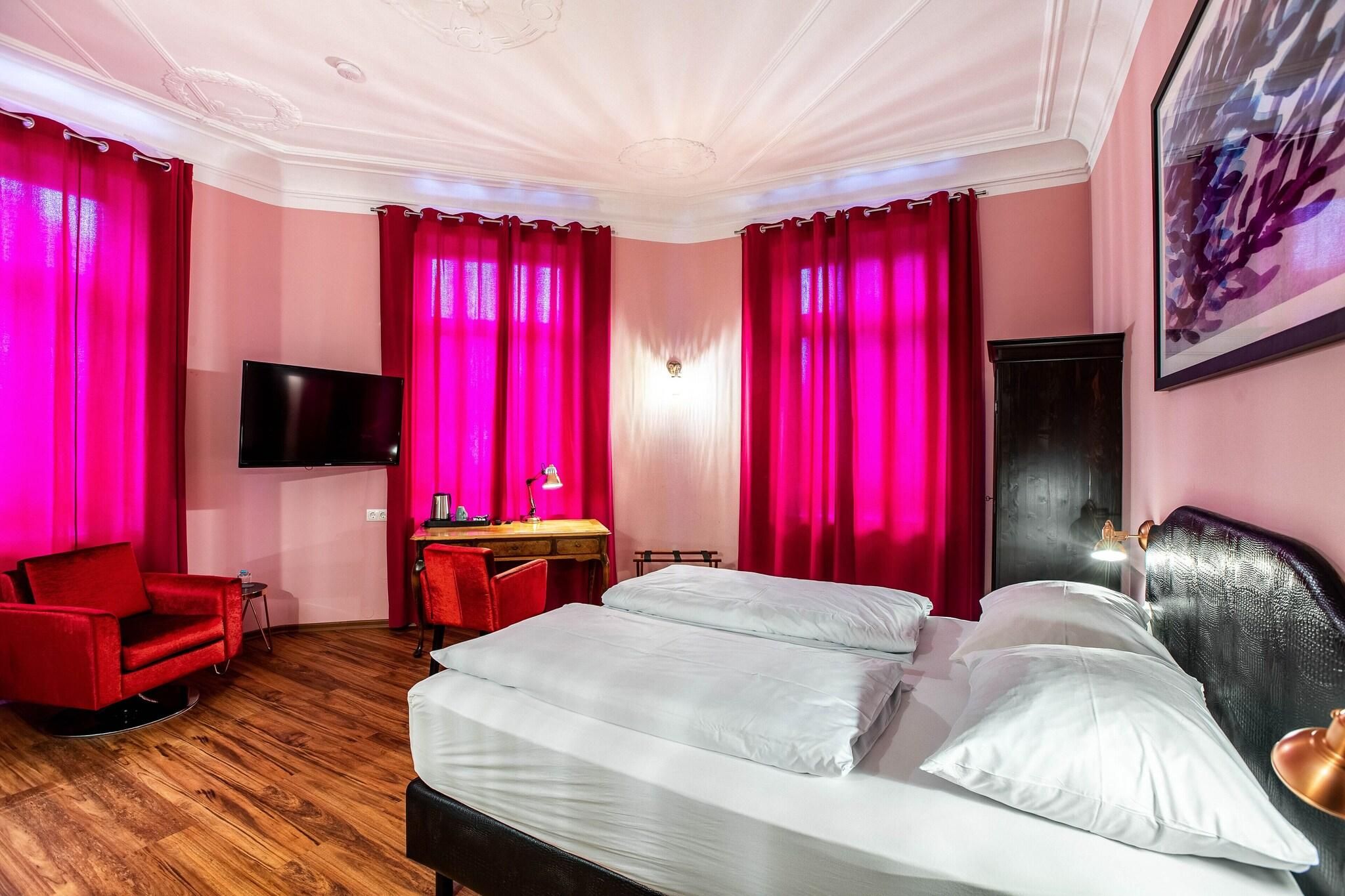 A hotel room with a bed, a desk, a chair, and a television.