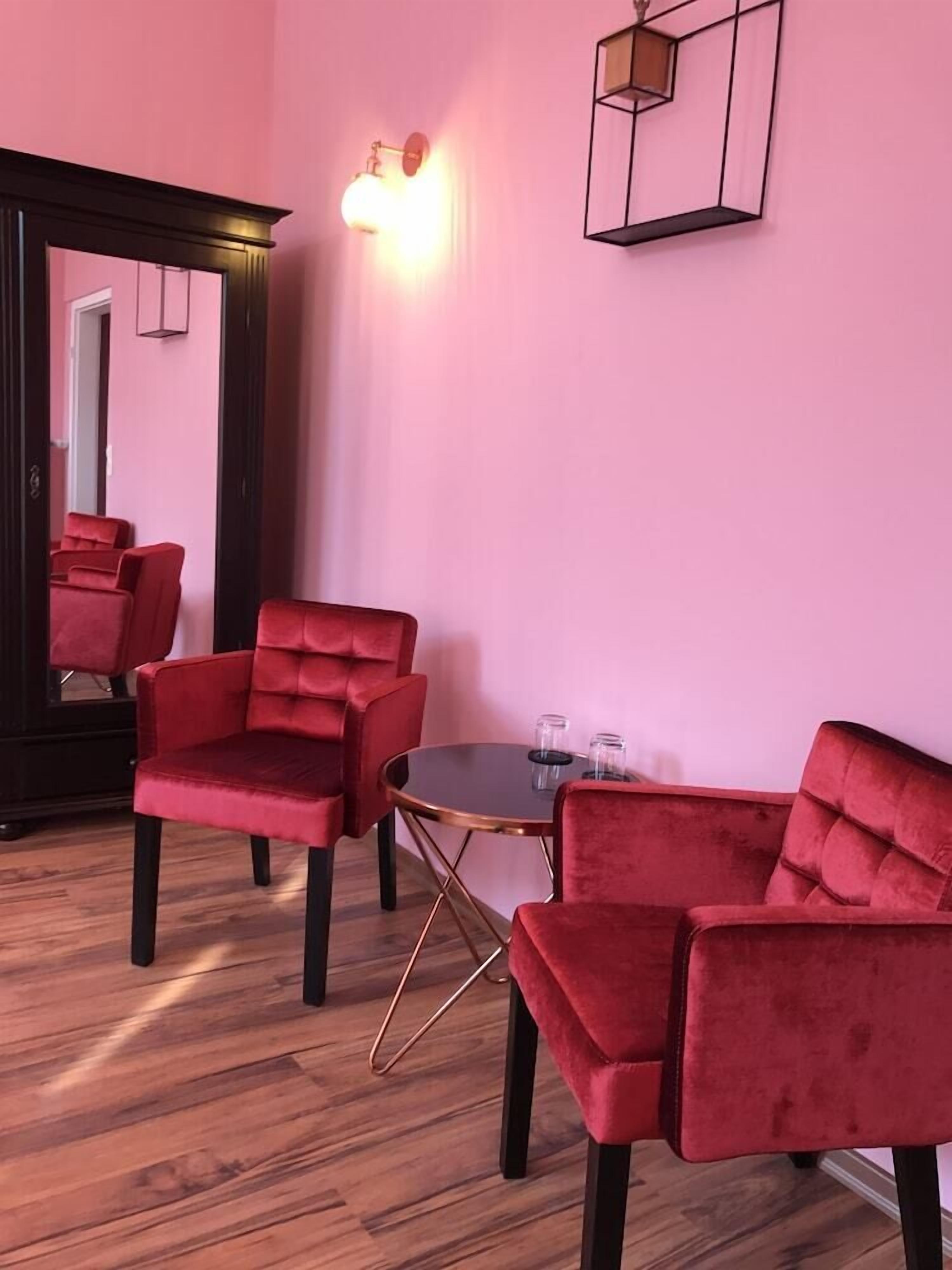 Una habitación con pared rosa, una mesa redonda y tres sillas rojas.