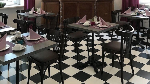 Comedor con piso a cuadros, mesas dispuestas con servilletas rosas y una araña.
