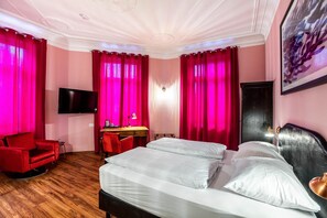 Een hotelkamer met een bed, een bureau, een stoel, een televisie en rode gordijnen.
