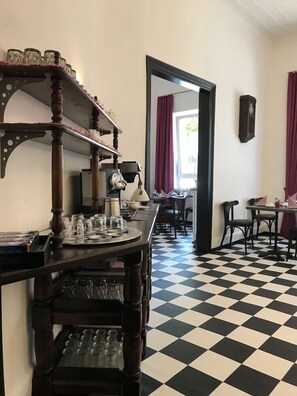 Een kamer met een geruite vloer, een houten tafel met verschillende objecten, een spiegel en een klok aan de muur.