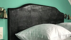 Una cama con un cabecero negro con textura, dos lámparas de noche y almohadas blancas.