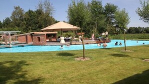 Una piscina con estructura de ladrillo, zona sombreada y área de césped con árboles.