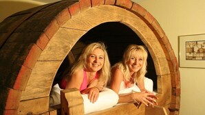 Dos personas en una estructura de madera rústica y arqueada, posiblemente una chimenea u horno, con un cuadro en la pared.