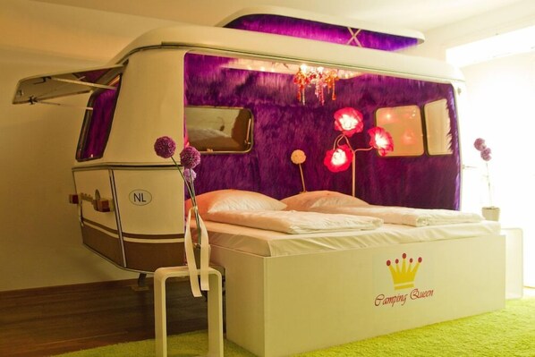 Una cama con dosel, una mesita y una silla en una habitación con pared morada y una ventana.