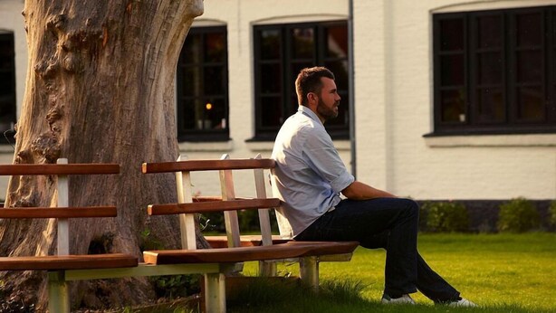 A man sitting on a bench in a park with a building in the background. - Aalbaek Badehotel, Sure Hotel Collection by Best Western (Aalbaek)