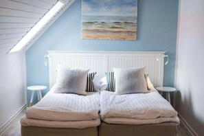 A bedroom with a sloped ceiling, a white headboard, two bedside tables, and a painting of a beach scene. - Aalbaek Badehotel, Sure Hotel Collection by Best Western (Aalbaek)