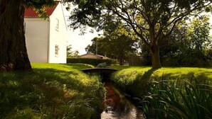 A serene garden with a small stream, lush greenery, and a white building with a red roof. - Aalbaek Badehotel, Sure Hotel Collection by Best Western (Aalbaek)