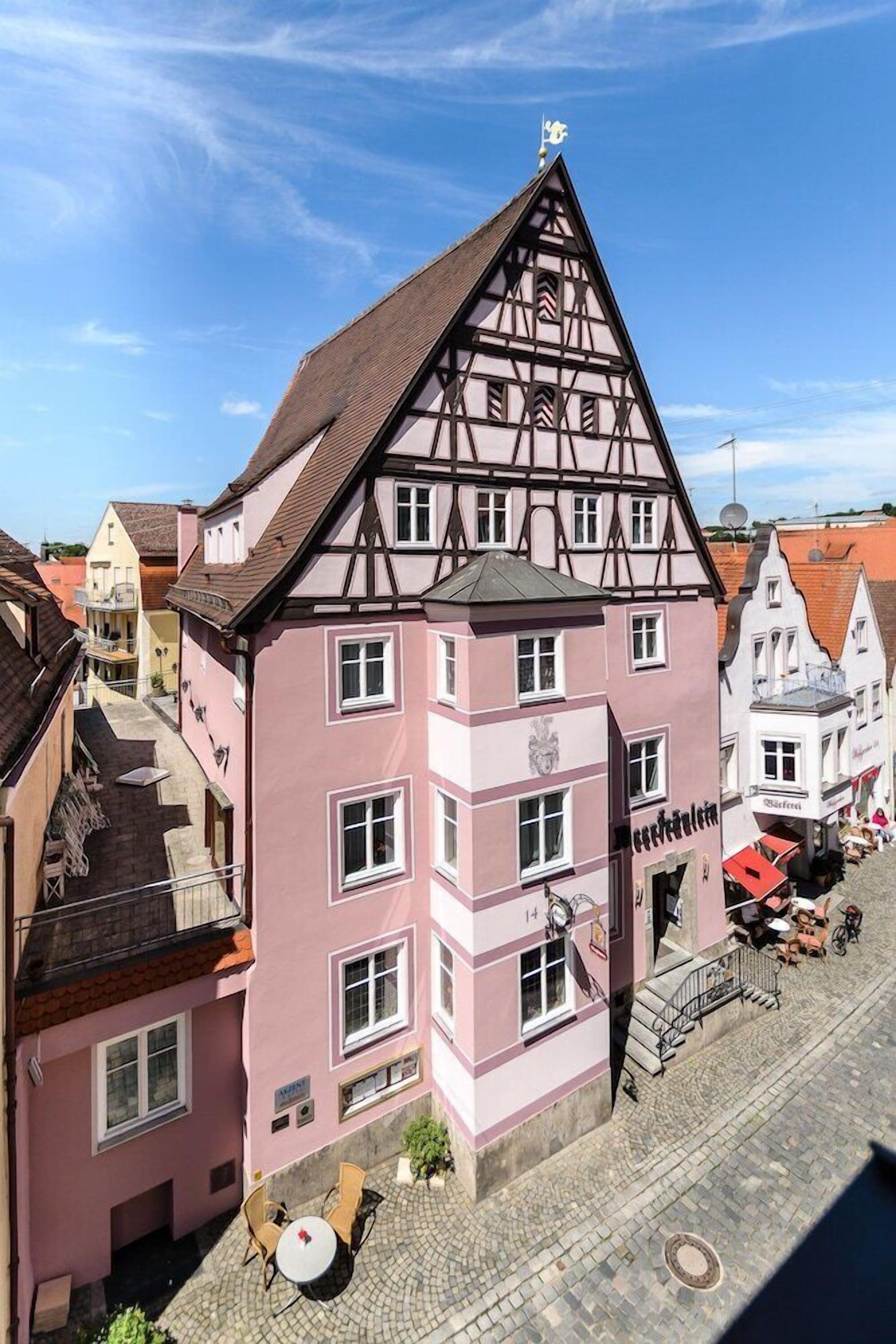 A pink building with a steeply pitched roof and a balcony.
