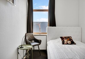 Una habitación de hotel con una cama, una silla, una mesita y un ventanal con cortinas.