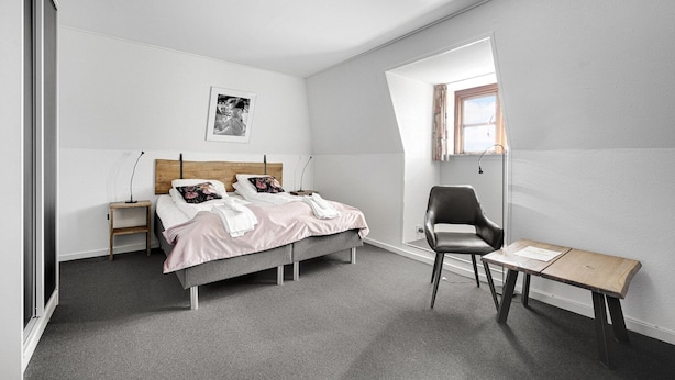 A bedroom with a bed, bedside tables, a chair, a small table, and a window. - Hotel Phnix Brnderslev (Bronderslev)