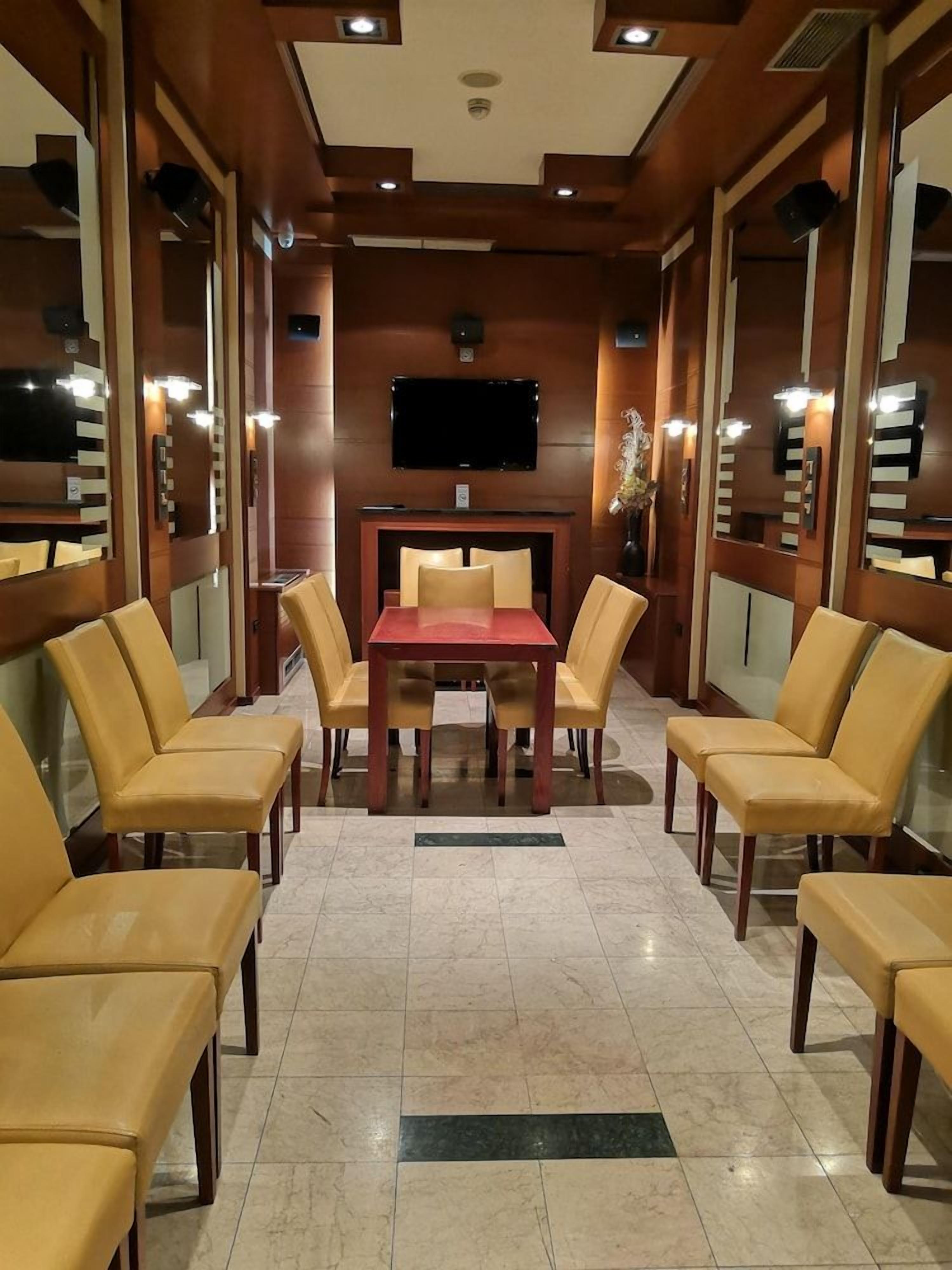 Un salón de conferencias con una mesa rectangular y seis sillas, un televisor de pantalla plana montado en la pared y paneles de madera en las paredes.