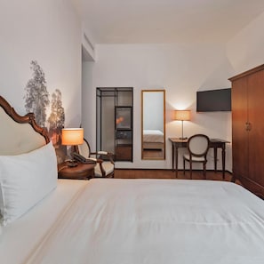 A hotel room with a bed, bedside table, lamp, chair, desk, mirror, wardrobe, and a wall-mounted TV. - Boutique Business Hotel La Tureta (Bellinzona)