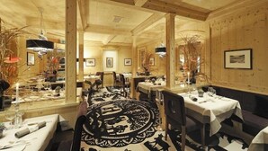 A restaurant with wooden interiors, round tables, and a central decorative rug. - Wellness Spa Hotel Ermitage (Saanen)