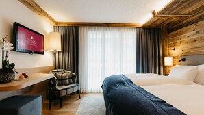 A hotel room with a bed, a desk, a chair, a TV, and a window with curtains. - Wellness Spa Hotel Ermitage (Saanen)