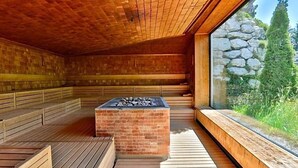 A sauna with wooden benches and a stone fireplace. - Wellness Spa Hotel Ermitage (Saanen)