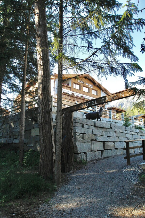 A stone wall with a wooden sign reading 'HOTEL SARAIN' and a building in the background. - TOP Hotel Sarain Active Mountain Resort (Lantsch-Lenz)