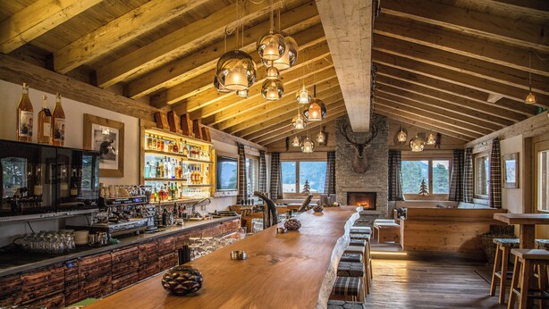 A bar area with wooden beams, a long counter, and a fireplace. - TOP Hotel Sarain Active Mountain Resort (Lantsch-Lenz)