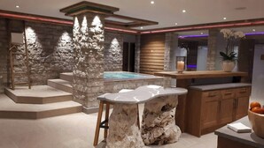 A modern interior with a stone wall, a hot tub, a wooden staircase, and a bar area. - TOP Hotel Sarain Active Mountain Resort (Lantsch-Lenz)