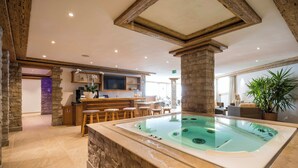 A spa area with a hot tub, wooden bar, and stone walls. - TOP Hotel Sarain Active Mountain Resort (Lantsch-Lenz)