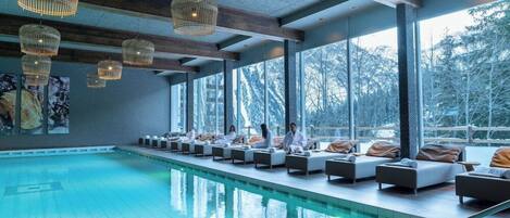 A modern indoor pool area with lounge chairs and a large window overlooking a snowy landscape.