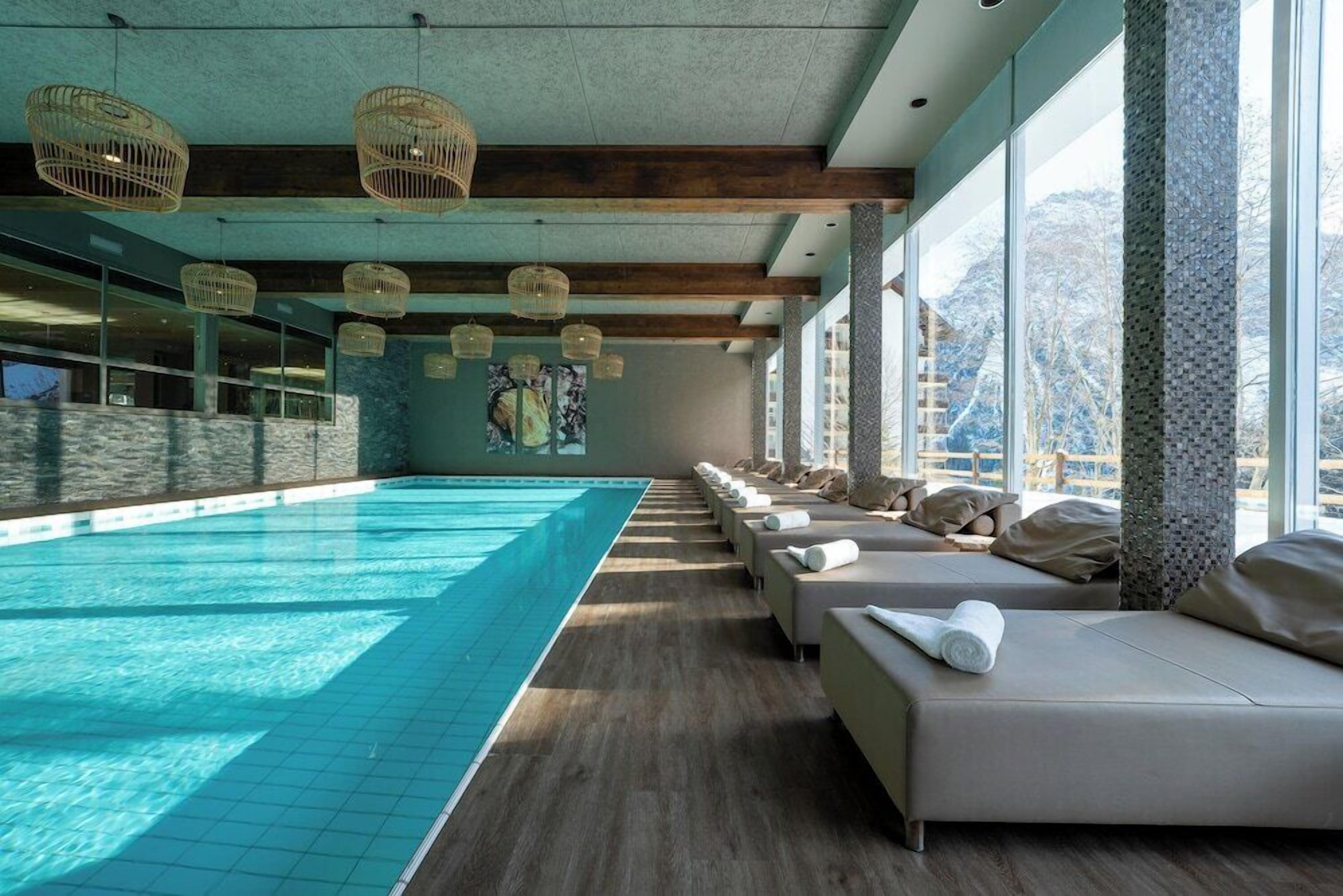 Un espace piscine doté d’un long banc le long du bord, de grandes fenêtres et de luminaires suspendus en osier au plafond.