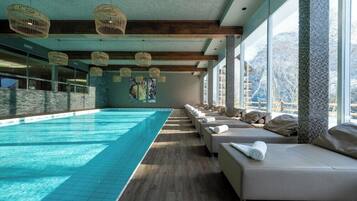 Un espace piscine doté d’un long banc le long du bord, de grandes fenêtres et de luminaires suspendus en osier au plafond.