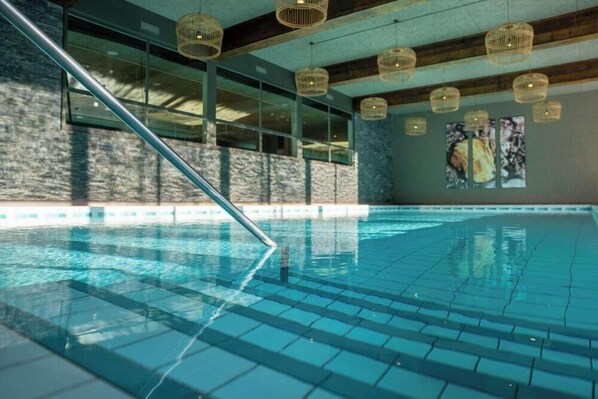 An indoor swimming pool with clear blue water, wooden beams, and hanging wicker light fixtures. - Robinson Club Arosa (Arosa)