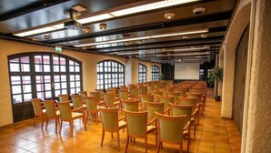 Une salle de conférence avec des rangées de chaises, de grandes fenêtres et un écran de projection.