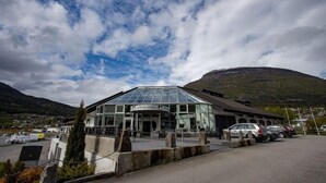 Un hôtel moderne doté d’une façade en verre, d’un parking et situé dans un cadre montagneux.