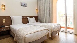 A hotel room with two beds, a nightstand, and a sliding glass door leading to an outdoor area. - Saoura Hotel Taghit (Taghit)