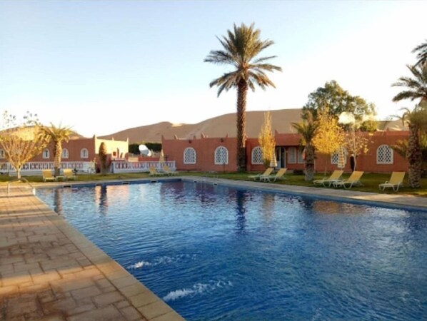 A swimming pool with lounge chairs and palm trees. - Saoura Hotel Taghit (Taghit)