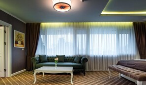 A room with a green sofa, a white coffee table, a brown bench, and a large window with sheer curtains. - Arpesos (Kardzali)