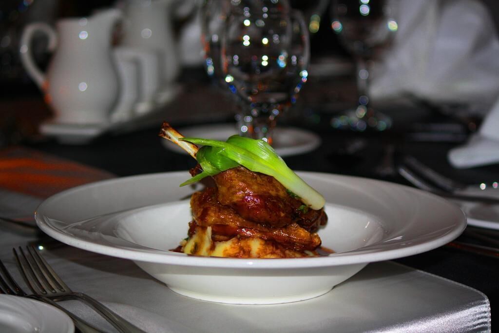 A white plate with a single piece of food, possibly a meat dish, garnished with a green vegetable.