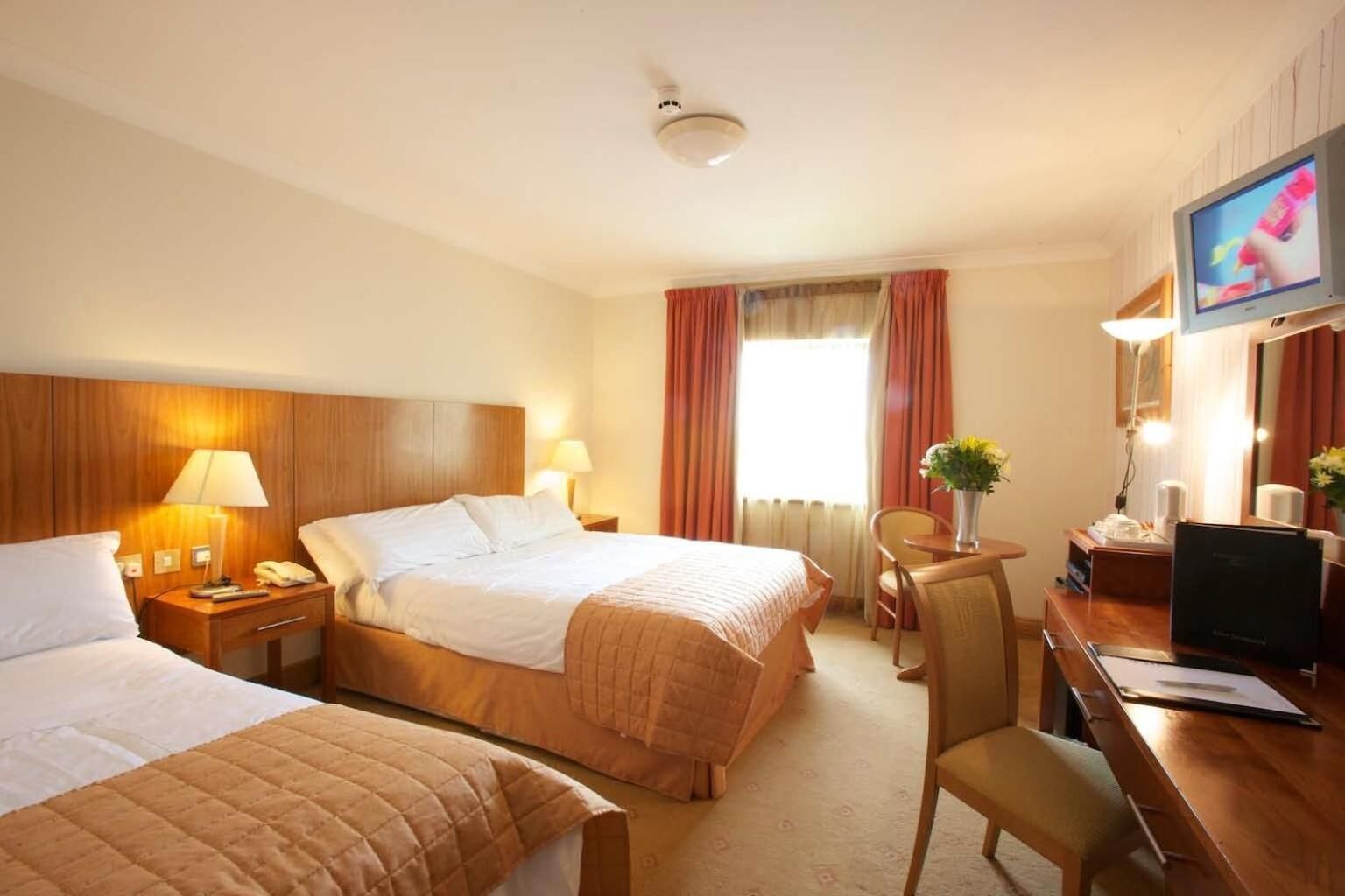 A hotel room with two beds, a desk, a chair, a TV, and a window with curtains.