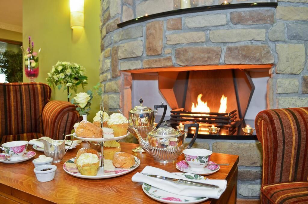 Une pièce chaleureuse avec une cheminée en pierre, une table dressée pour le thé de l’après-midi, agrémentée de pâtisseries et de théières, et des fauteuils à rayures.