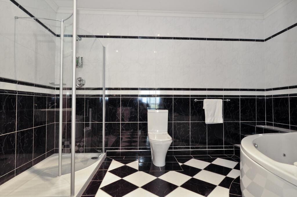 A bathroom with a black and white checkered floor, a glass shower enclosure, a white toilet, and a bathtub.