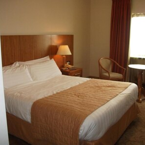 A hotel room with a large bed, a bedside table with a lamp, a chair, and a small round table. - Broadhaven Bay Hotel (Belmullet)