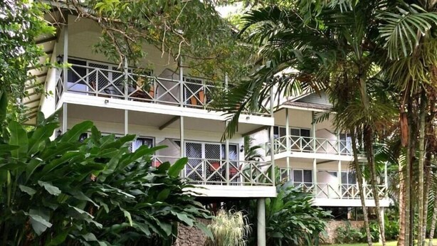 Un hotel de varios pisos con balcones, rodeado de abundante vegetación.