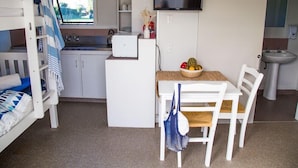 Ein kleines Zimmer mit Etagenbetten, einer Küchenzeile, einem Esstisch mit Stühlen, einem Fernseher und einem Waschbecken.