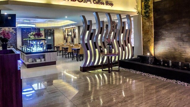 Uma Cafeteria AMBOJA com interior moderno, incluindo uma área de recepção com parede decorativa e uma área de estar com mesas e cadeiras.
