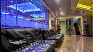 Um lobby com sofás de couro preto, uma escadaria e uma parede de vidro com plantas.