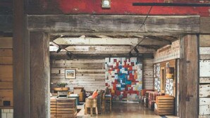 Un interno rustico con pareti in legno, un'opera d'arte geometrica dai colori vivaci e un piccolo angolo salotto con sgabelli e un tavolo.