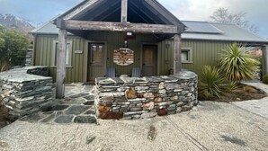Una baita rustica con fondamenta in pietra, un portico in legno e un cartello che indica che si tratta di una località "Cabbage Tree".