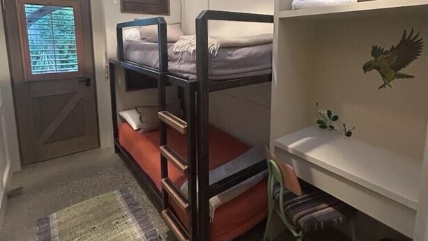 Una camera con un letto a castello, una scrivania, una sedia, una finestra con persiane e una porta.